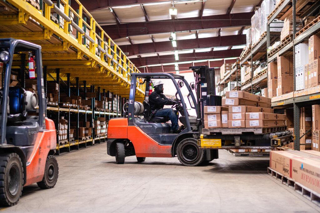 A forklift driver in a warehouse moving boxes to a different area.