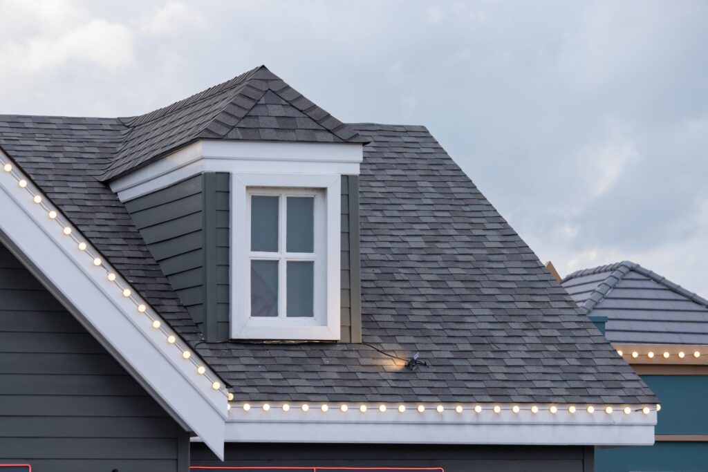 A grey shingled roof with lights around the gutters.