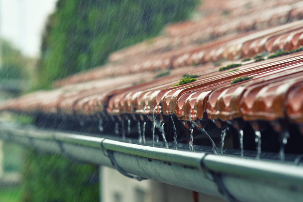 Rain falling off a terracotta roof into a rain gutter.