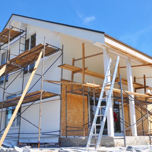 A home's exterior under construction with scaffolding and ladders set up.